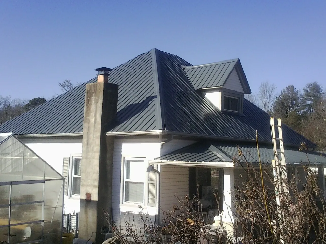 Dark blue standing seam metal roof on a white farmhouse with dormer — Slate & Tile Roof Repair by Roofing Brothers in Raymondville