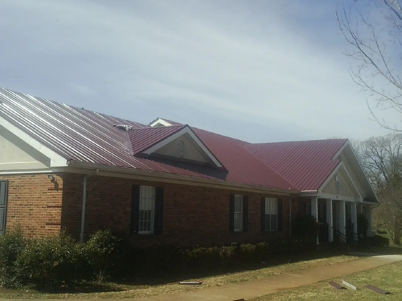 Red metal roof with gabled entries on a long brick building, from a Hail Damage Roof Repair job in Raymondville