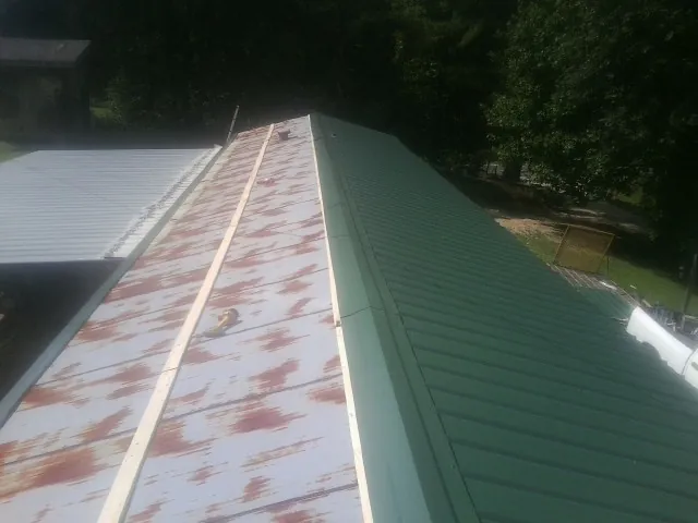 Old rusted panels beside newly installed green metal roofing — Wind Damage Roof Repair by Roofing Brothers in Raymondville