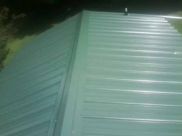 New green metal panels meeting at the ridge of a roof — Flat Roof Repair work by our crew in Raymondville