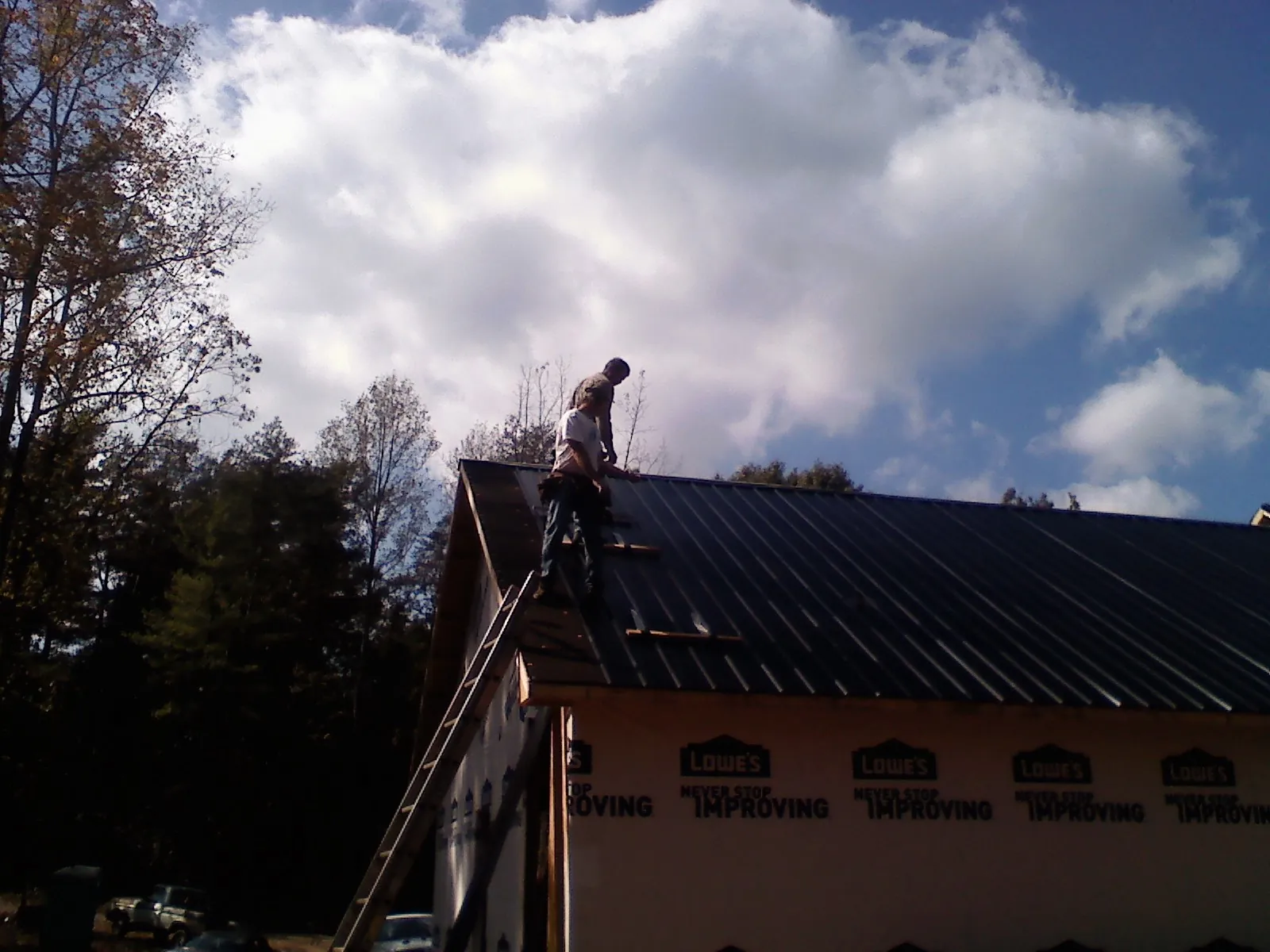 Roofer fastening dark metal panels high against a cloudy sky, from a Roof Inspection job in Raymondville