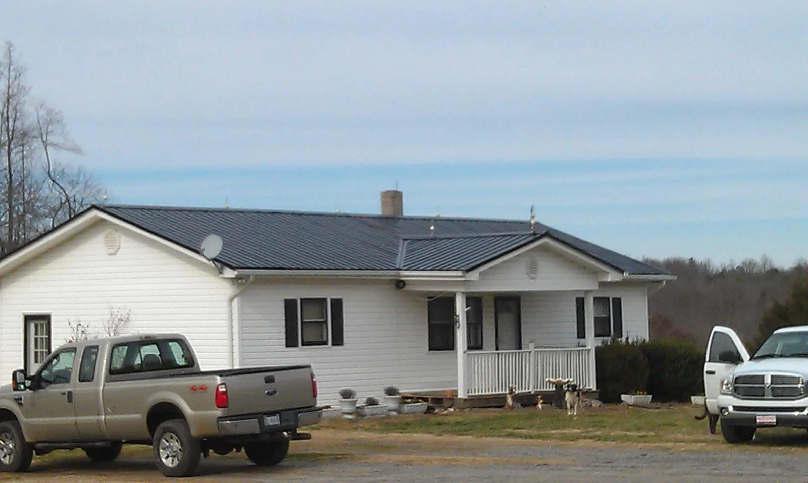 Finished dark metal roof on a white ranch home with work trucks parked in Raymondville