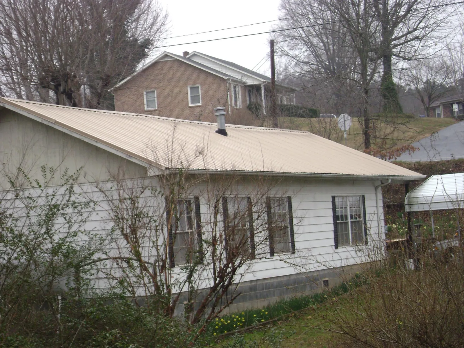 Tan metal roof on a white sided house set into a hillside — Commercial Roofing by Roofing Brothers in Raymondville