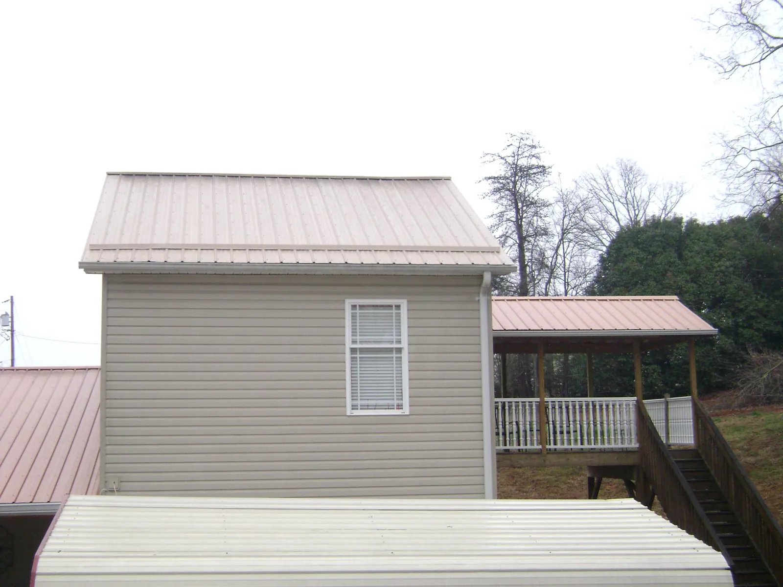 Tan metal roofs on a two story addition and attached porch, from a Roof Replacement job in Raymondville
